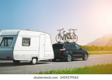 Black suv with bicycles mounted on top tows a white caravan on a road trip with scenic mountains in the background