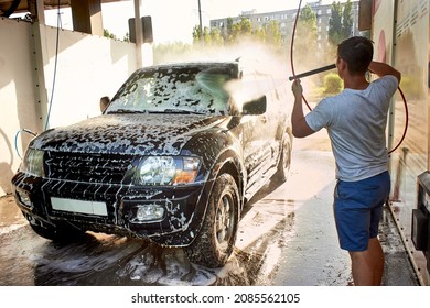 A black SUV car at a self-service car wash. Washing the car with your own hands. A black car in cleaning foam. A man washes his auto during the day, washes of the foam.