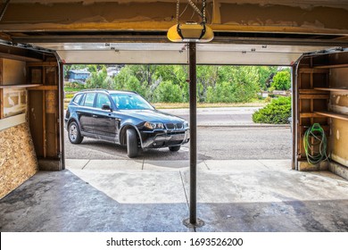 Black Suv Turning Into Garage With Automatic Overhead Door Opener - Grainy Unfinished Surfaces And Pavement - Suburban Neighborhood With Trees