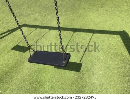 Black swing on green grass at the playground. Green coating on the sports ground. Place to add text