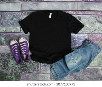 Black T Shirt Mockup Flat Lay On Purple Brick Background With Purple Shoes And Ripped Jeans
