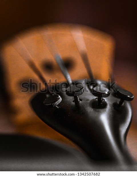 Black\
tailpiece and fine tuners of a violin. It\'s a macro photo. Strings\
and bridge are visible in the background. Close\
up.