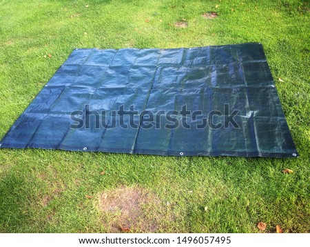 Black tarpaulin tarps spread as ground sheet on grass lawn at campsite