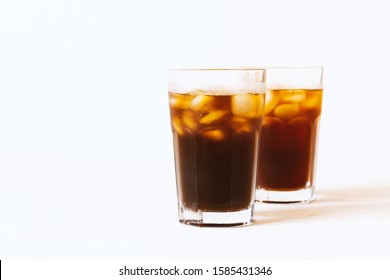 Black tea, coffee or cola with ice in glass on white background. Horizontal photo with copy space. Two glass with drink on table. Summer beverage