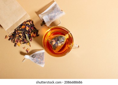 Té negro, hierbas y fruta elaborada en una taza transparente. Té para prepararse en bolsos de té. El concepto de una bebida natural saludable. Bolsas de té sobre fondo beige
