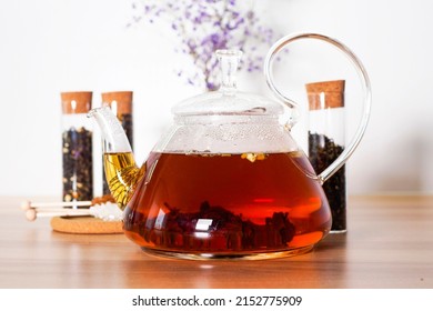 Black tea with herbs and berries in a transparent teapot on a white table. Jar with loose leaf tea. Hot brown drink. Advertising tea company, concept, presentation.