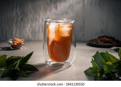 Black tea with mint oil near mint leaves in a double-walled glass Cup.