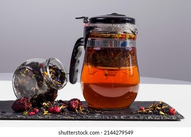 Black tea with taiga herbs. Glass teapot on the table with dry tea by weight. Hot drink of beautiful tea color. Storage conditions, rules and method of brewing.