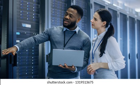 Black IT Technician with a Laptop Computer Gives a Tour to a Young Intern. They Talk in Data Center while Walking Next to Server Racks. Running Diagnostics or Doing Maintenance Work. - Shutterstock ID 1319513675