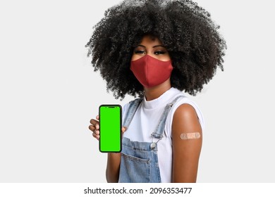 Black Teen Girl Holding Cell Phone Next To Her Arm With Vaccine Sticker, She Wears Face Shield, Cell Phone Screen In Green Chroma Key