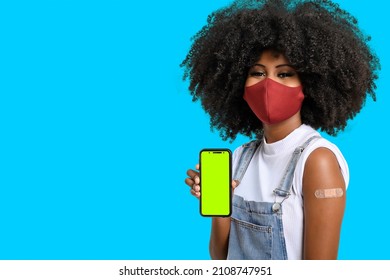 Black Teen Girl Holding Cell Phone Next To Her Arm With Vaccine Sticker, She Wears Face Shield, Cell Phone Screen In Green Chroma Key