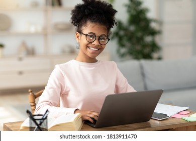 Black Teen Girl At Laptop Learning Online Smiling To Camera Sitting At Table At Home, Wearing Eyeglasses. Distant School Education