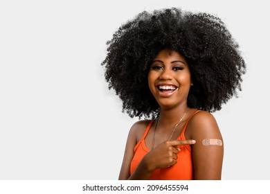 Black Teen Girl Smile And Points To Her Arm With Vaccine Sticker, She Does Not Wear Face Shield, Isolated On Gray Background.