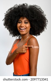 Black Teen Girl Smile And Points To Her Arm With Vaccine Sticker, She Does Not Wear Face Shield, Isolated On Gray Background.