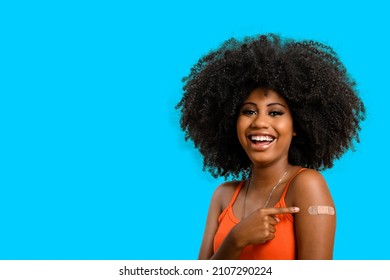 Black Teen Girl Smile And Points To Her Arm With Vaccine Sticker, She Does Not Wear Face Shield, Isolated On Gray Background.