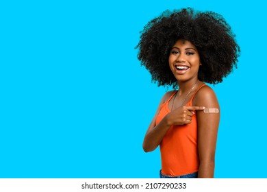 Black Teen Girl Smile And Points To Her Arm With Vaccine Sticker, She Does Not Wear Face Shield, Isolated On Gray Background.