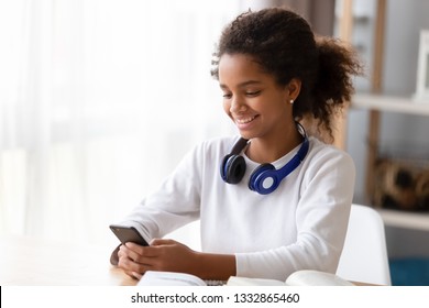 Black teen girl studying use training materials books she distracted from learning holds mobile phone chatting with friend surfing internet. Generation addicted with gadgets everyday overuse concept