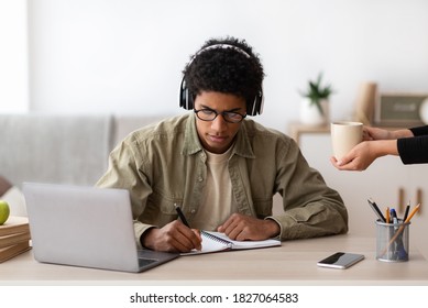 Black teen guy in headphones studying online from home, making notes in copybook. Teenage student learning remotely on laptop, doing home assignment, watching video lesson - Shutterstock ID 1827064583