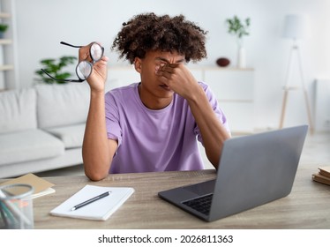 Black Teen Guy Rubbing Tired Eyes, Sitting At Desk With Laptop Computer, Exhausted From Studying Online. Afro Teenager Having Sight Fatigue From Distance Learning, Looking At Screen Too Long