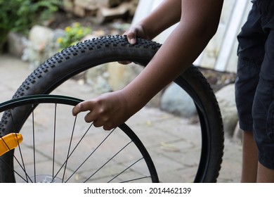 A Black Teenage Boy Repairing A Flat Bike Tyre