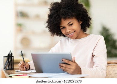 Black Teenager Girl Using Tablet Computer Learning Distantly Online Sitting At Desk At Home. Web Education And E-Learning