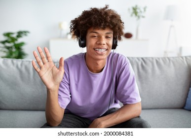 Black Teenager Talking To His Friend Or Family Online, Wearing Headphones And Waving At Camera From Home. Cheerful African American Adolescent Having Web Conference, Chatting To Someone Remotely