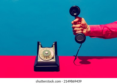 Black telephone. Retro objects, gadgets. Female hand holding handset of vintage phone isolated on blue pink background. Vintage, retro 80s, 70s style. Complementary colors. Copy space for ad, design