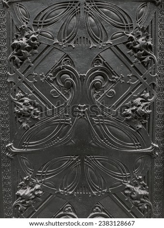 A black, textured gothic wall in Chicago, its intricate details and dark aesthetic highlighted by the stark contrast of broad daylight