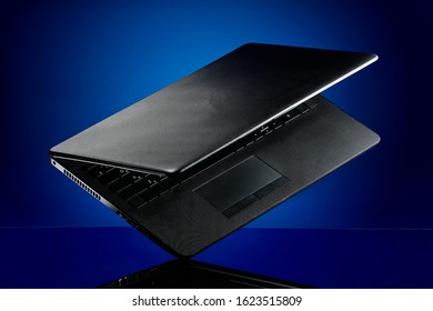 A Black Textured Laptop Flies Over The Table In The Air On A Dark Blue Background