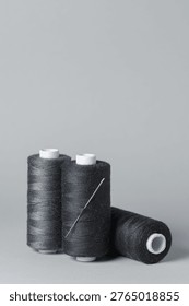 Black thread spools with needle close-up on white background with copy space for text