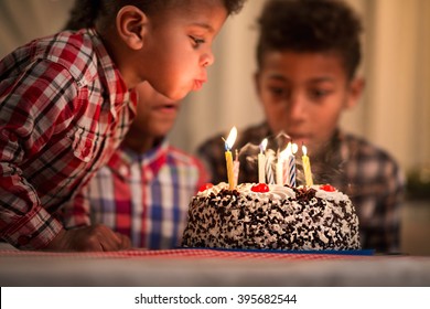 Black toddler blowing candles out. Child blows birthday candles out. Youngest brother's birthday. Spending festive time together.