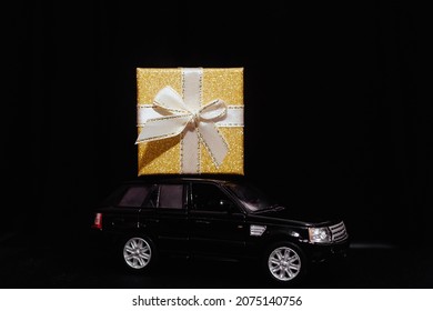 black toy car carries a gift. Gold box with ribbon. Concept of Christmas mood and preparation for the celebration. Discounts. Present. Black Friday. 2024. Seasonal sale, big discounts