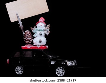 Black toy car is carrying a snowman and a sign. The concept of Christmas mood and preparation for the celebration. Discounts present. Black Friday. 2024. Seasonal sale, big discounts