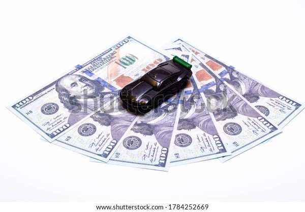 Black toy car on a heap of dollar bills on a white\
and black background. A sports car with a green spoiler, a wing on\
dollars in a close-up top and side view. Rear and front car.\
Selling, buying
