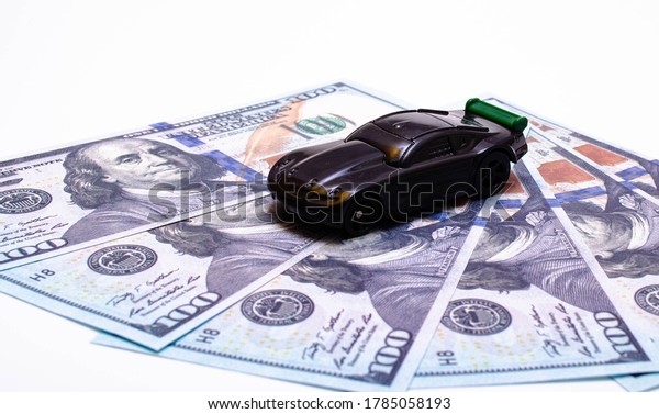 Black toy\
car on a heap of dollar bills on a white and black background. A\
sports car with a green spoiler, a wing on dollars in a close-up\
top and side view. July 2020. Los\
Angeles.USA\
