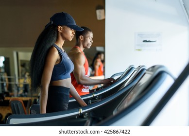 Black Trainer And Sexy African American Woman On The Treadmill In Gym. Fitness Concept