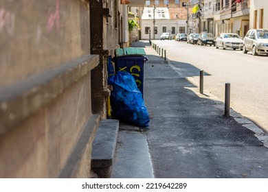 Black Trash Bin With A Large Blue Plastic Bag Next To It In An Urban Residential Area