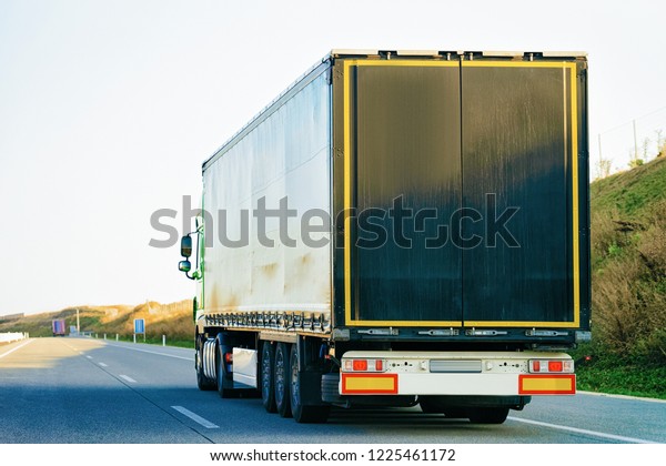 Black Truck in the asphalt road of\
Poland. Lorry transport delivering some freight\
cargo.
