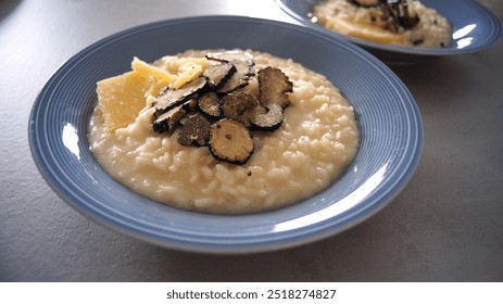 Black truffle risotto, parmesan cheese risotto, two blue dishes, lunch for two, with a drop of olive oil, on a gray table, side view, Italy - Powered by Shutterstock