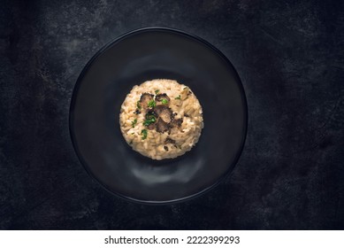 Black truffle risotto recipe.  Autumn creamy consistency risotto in stylish black dish on the black background. Dark autumn or winter mood, style of the Chef's table, top view, one dish 