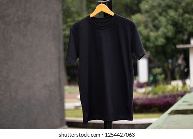 Black t-shirt on wood hanger in outdoor. black t shirt short sleeve ready for your mock up design or presentation your design project.