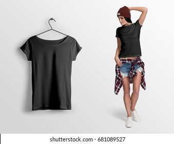 Black T-shirt On A Young Woman In Shorts, Hat And Checked Shirt, Isolated, Mockup. Hanging Black Blank T-shirt, Against Empty Wall.