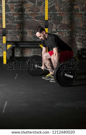 Black t-shirt and red short male athlete practicing olympic lifts at gym with brick wall background.