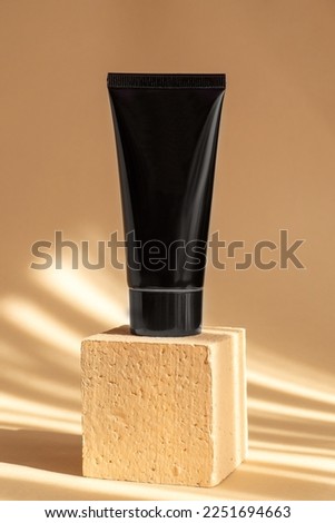 Black tube of face cream on square platform in sunlight. Container for lotion, gel, shaving foam, toothpaste on brown background. Mockup of branding of cosmetic product. Vertical image