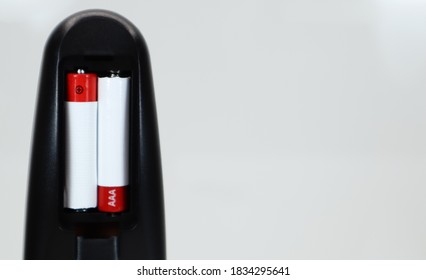 Black TV remote control with AAA alkaline batteries in red and white on a white background. Battery replacement, spare parts. Remote control battery compartment close-up. Copy space