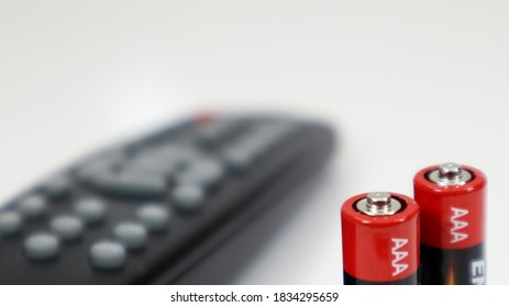 Black TV remote control with AAA alkaline batteries in red and white on a white background. Battery replacement, spare parts. Remote control battery compartment close-up.