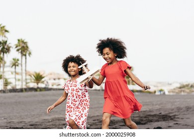 Black Twin Sisters Running On The Beach While Playing With Wood Airplane - Focus On Faces