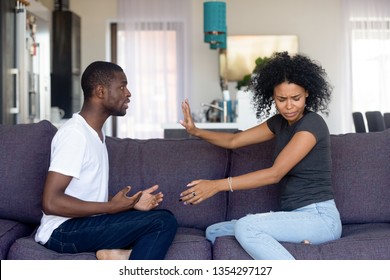 Black Unhappy Couple Having Quarrel At Home Arguing Sitting On Sofa In Living Room At Home, Husband Makes Excuses Wife Refuses Listen Dont Believe Him. Cheating, Problems, Fed Up And Break Up Concept