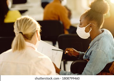 Black university student and her friend wearing protective face masks while going through test results in the classroom. 
