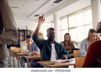 Black university student raising his arm to answer a question while having class in the classroom.